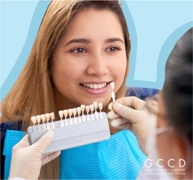 Dentist matching tooth shade guide to a smiling woman’s teeth during a cosmetic dentistry consultation.
