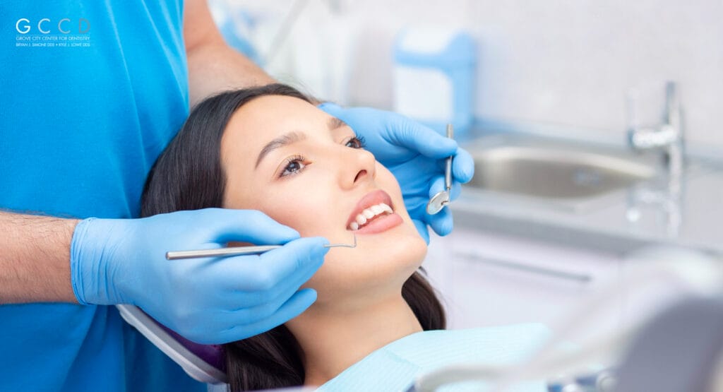 A woman sitting in a dental chair during a checkup, with a dentist gently examining her teeth, symbolizing routine oral care without using a dental mirror.