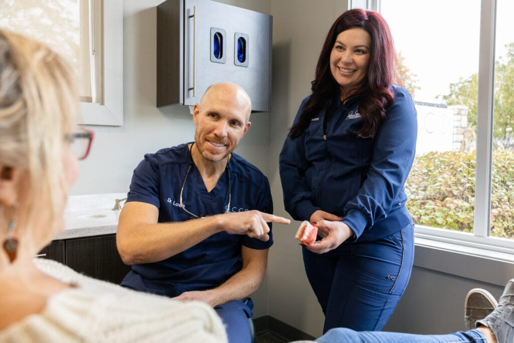 Dr. Kyle Lowe pointing to a teeth model held by a dental assistant while explaining the procedure to a patient